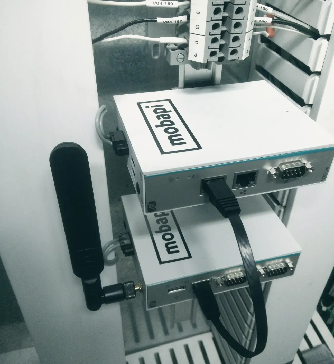 Deux Mobapi.BOX empilées dans une armoire électrique, sous un bornier, avec une antenne et un câble réseau.