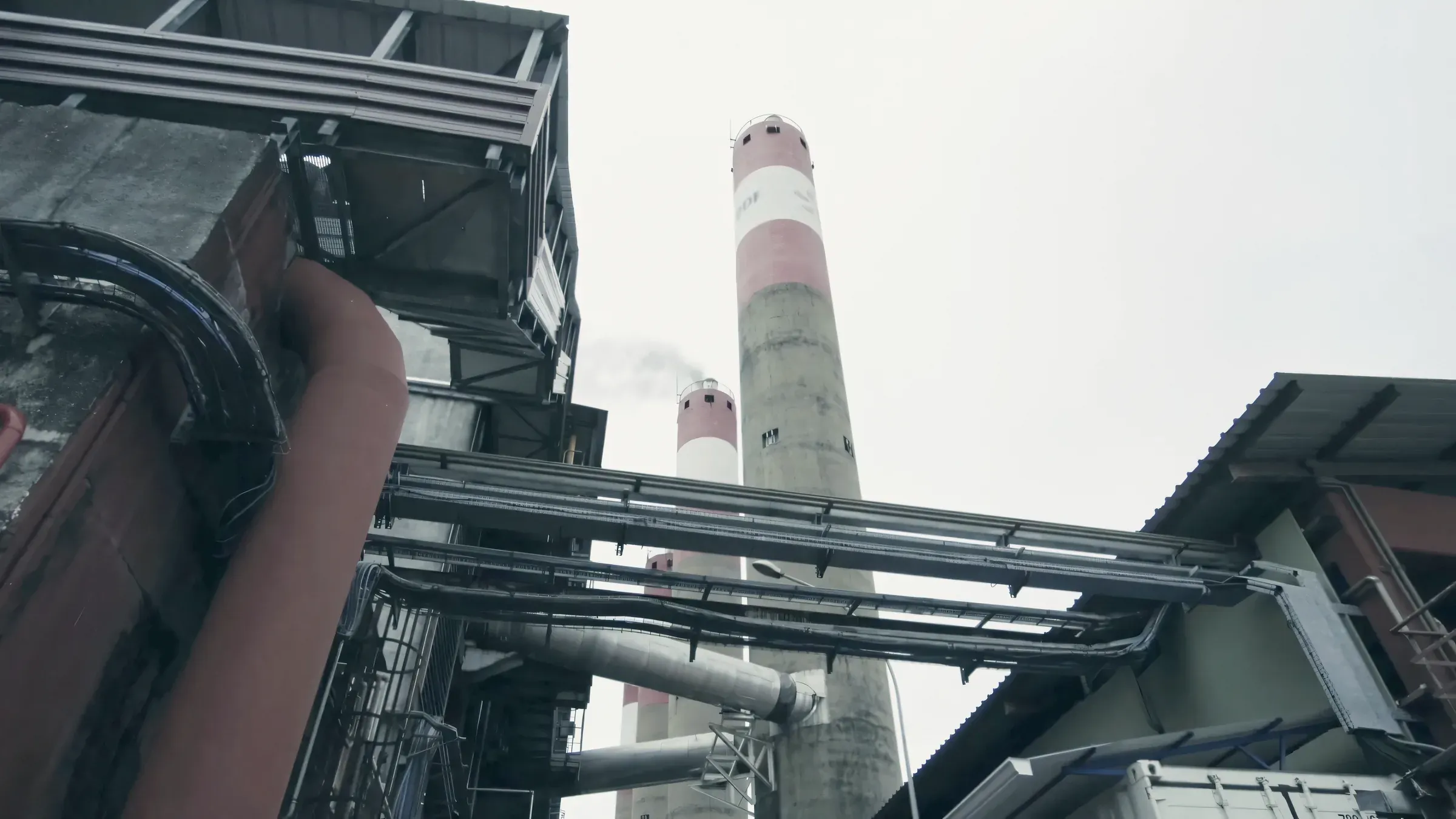 Deux cheminées rayées de rouge et de blanc derrière les tuyauteries d’une centrale thermique.