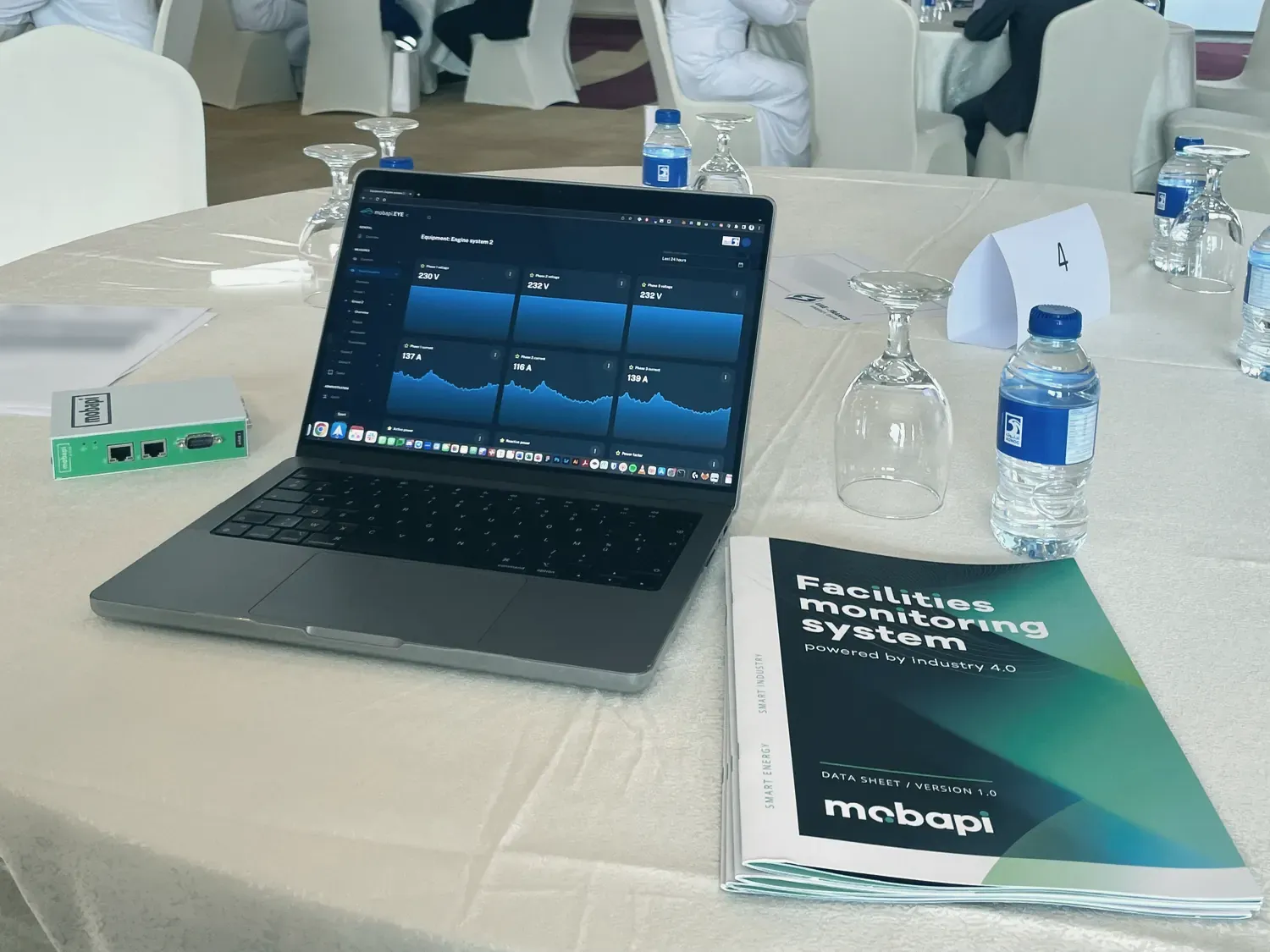 Sur la table de Mobapi, un ordinateur ouvert sur un tableau de bord, une Mobapi.BOX verte et une brochure.