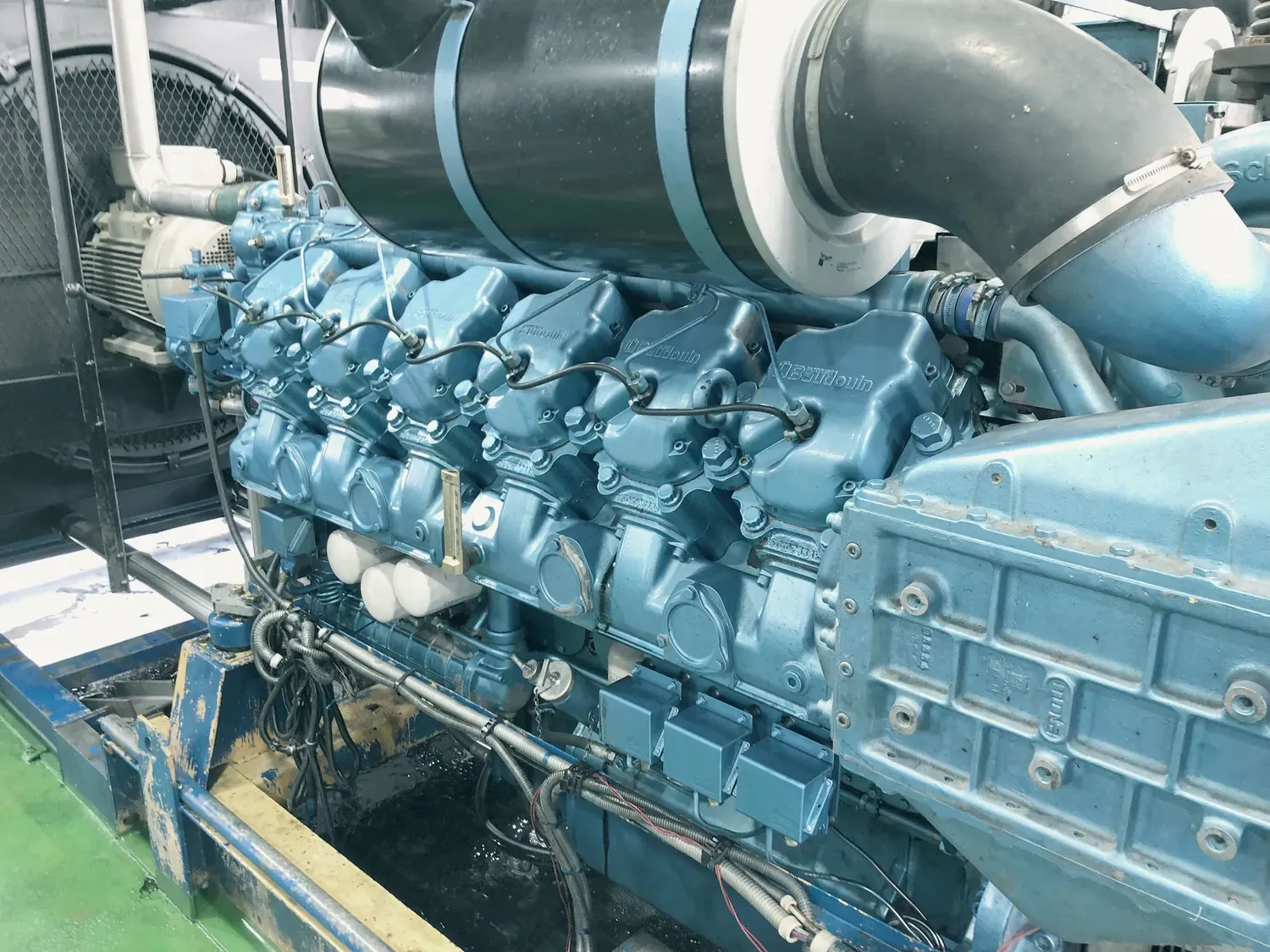Le moteur diesel bleu d’un groupe électrogène, vu de près : culasses, tuyauteries et gaine d’échappement.