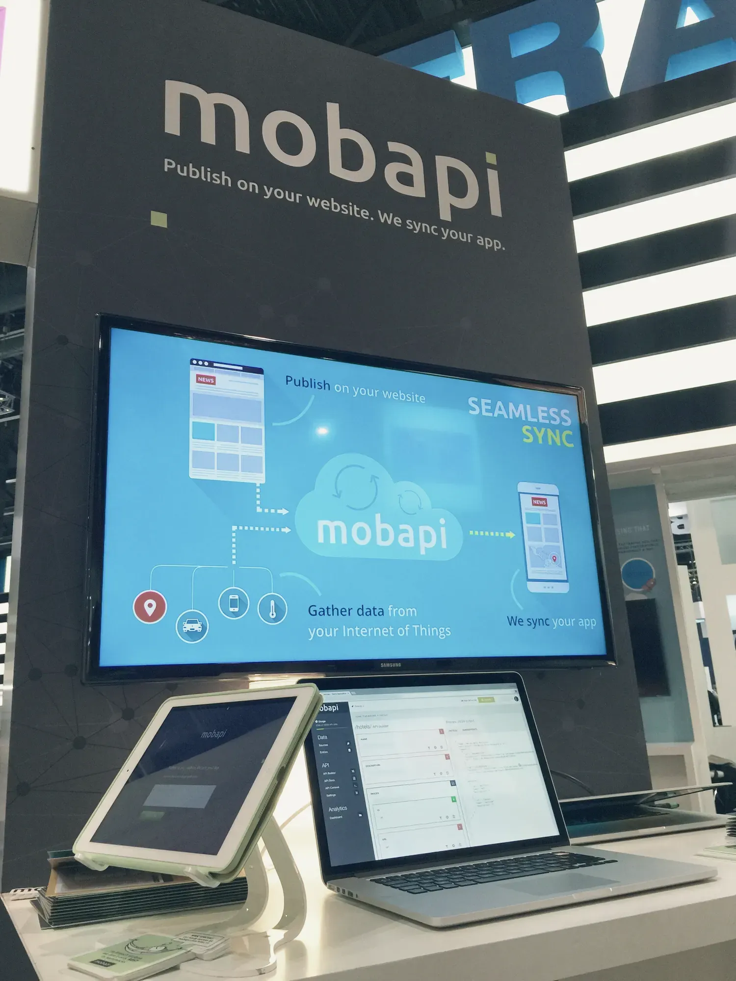 Le stand de Mobapi : sous le logo, un grand écran explique le fonctionnement de la plate-forme ; devant, une tablette et un ordinateur portable en démonstration.