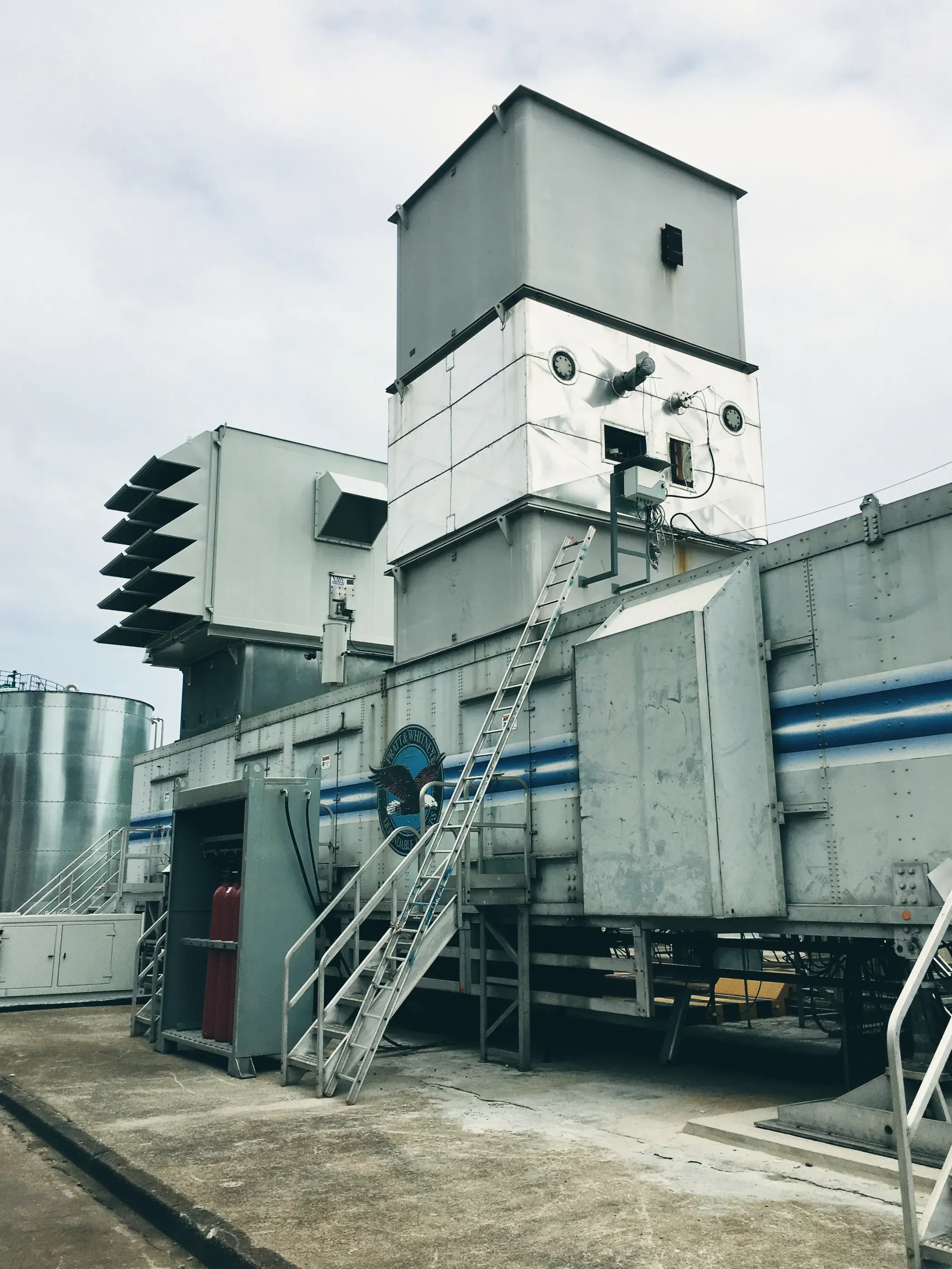 Le caisson d’une turbine à combustion, avec ses escaliers d’accès et sa prise d’air en hauteur. Derrière, à gauche, des cuves de stockage.