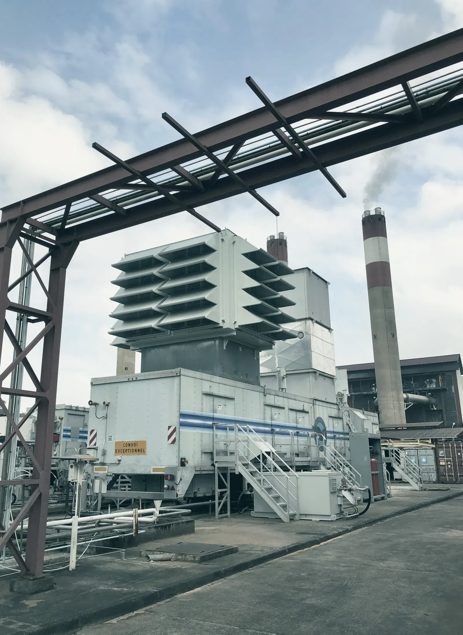 Turbine à combustion d’une centrale thermique d’EDF équipée par Mobapi, sous un portique de tuyauteries, cheminée en arrière-plan.